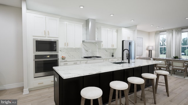 42096 Picasso Sq, Ashburn, VA 20148 - kitchen featuring appliances with stainless steel finishes, wall chimney range hood, a sink, an island with sink, and light wood-style floors