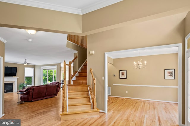 10604 Sourwood Ct, Laurel, MD 20723 - staircase with a ceiling fan, wood finished floors, crown molding, a glass covered fireplace, and a chandelier