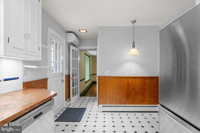 28 The Strand, New Castle, DE 19720 - kitchen with stainless steel appliances, a baseboard heating unit, a wall unit AC, white cabinetry, and a wainscoted wall