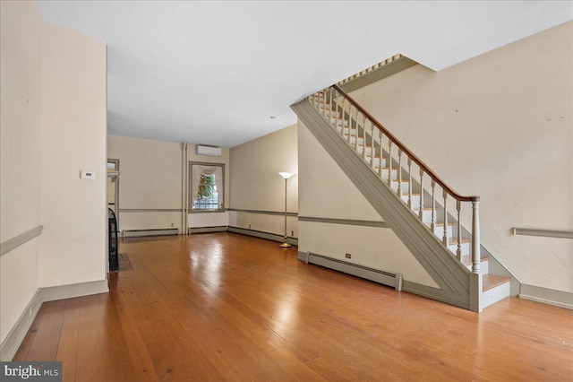 28 The Strand, New Castle, DE 19720 - unfurnished living room featuring baseboard heating, hardwood / wood-style flooring, stairs, baseboards, and a wall mounted AC