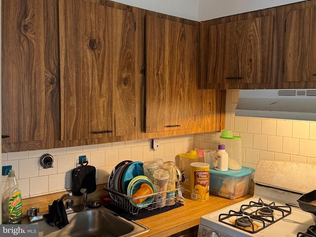 4029 Cedardale Rd, Baltimore, MD 21215 - kitchen featuring under cabinet range hood, white gas range oven, backsplash, light countertops, and a sink