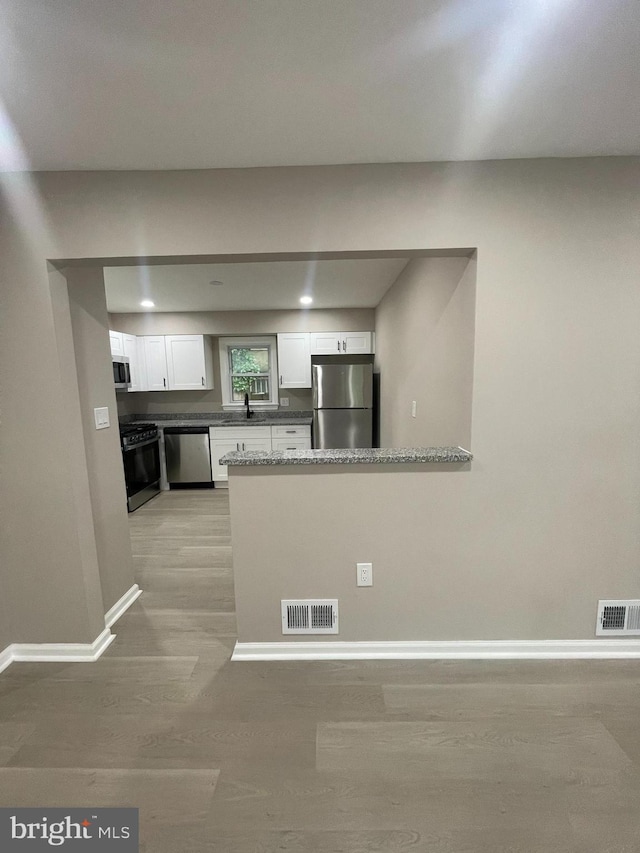 5010 54th Ave, Hyattsville, MD 20781 - kitchen with appliances with stainless steel finishes, light wood finished floors, baseboards, white cabinetry, and a peninsula