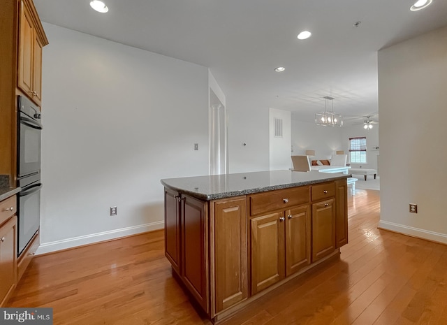 24655 Broad Creek Dr, Hollywood, MD 20636 - kitchen featuring brown cabinets, light wood-style floors, baseboards, a center island, and dark stone countertops