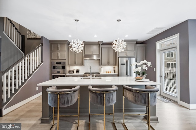 141 Center St S Unit 6, Vienna, VA 22180 - kitchen with stainless steel appliances, under cabinet range hood, a chandelier, gray cabinets, and decorative backsplash