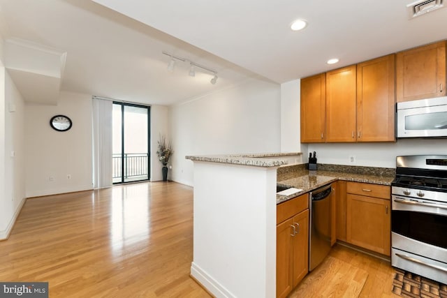 414 Water St Unit 3006, Baltimore, MD 21202 - kitchen with appliances with stainless steel finishes, a peninsula, brown cabinetry, rail lighting, and light wood-type flooring