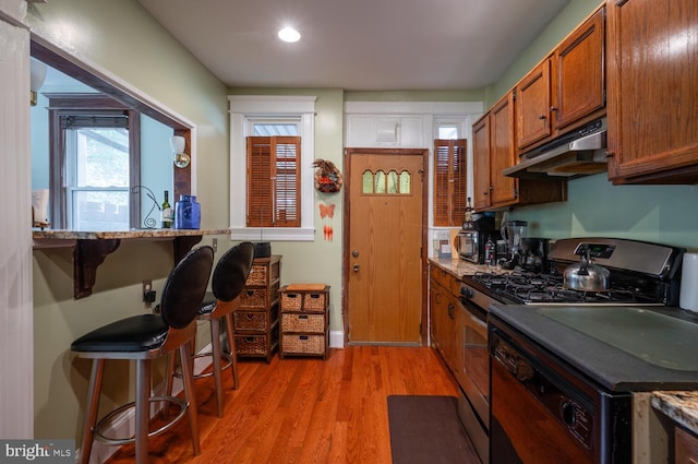 4800 Illinois Ave NW, Washington, DC 20011 - kitchen featuring under cabinet range hood, stainless steel gas range oven, brown cabinetry, light wood-style floors, and a breakfast bar