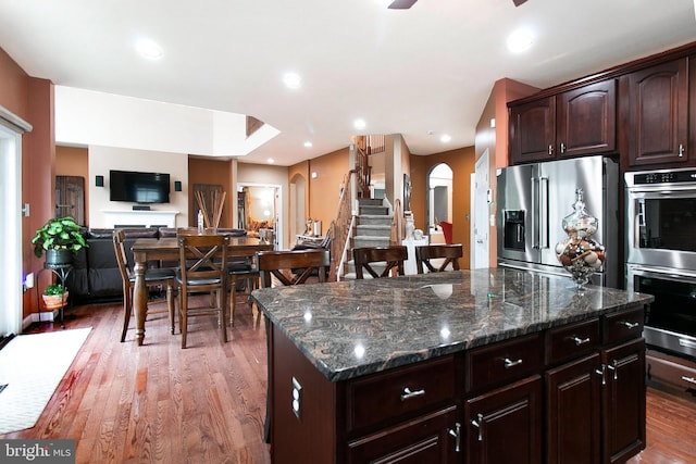 13763 Deacons Way, Gainesville, VA 20155 - kitchen featuring appliances with stainless steel finishes, light wood-style flooring, a center island, dark brown cabinetry, and dark stone counters
