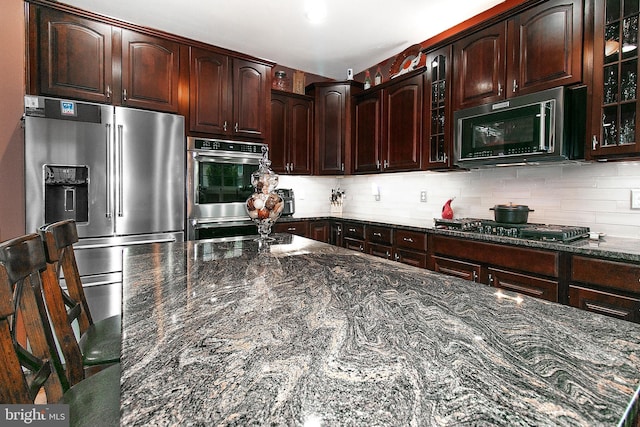 13763 Deacons Way, Gainesville, VA 20155 - kitchen with appliances with stainless steel finishes, dark stone countertops, glass insert cabinets, and backsplash