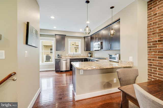 585 Regent Pl NE, Washington, DC 20017 - kitchen with appliances with stainless steel finishes, a peninsula, dark wood-style floors, light stone countertops, and a sink
