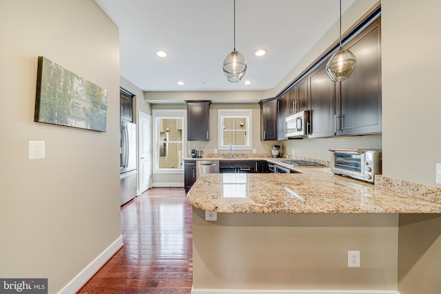 585 Regent Pl NE, Washington, DC 20017 - kitchen with appliances with stainless steel finishes, light stone counters, a peninsula, dark brown cabinets, and hardwood / wood-style flooring
