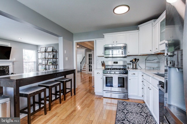 812 Red Rock Cir, Royersford, PA 19468 - kitchen featuring appliances with stainless steel finishes, white cabinets, tasteful backsplash, light wood finished floors, and a fireplace