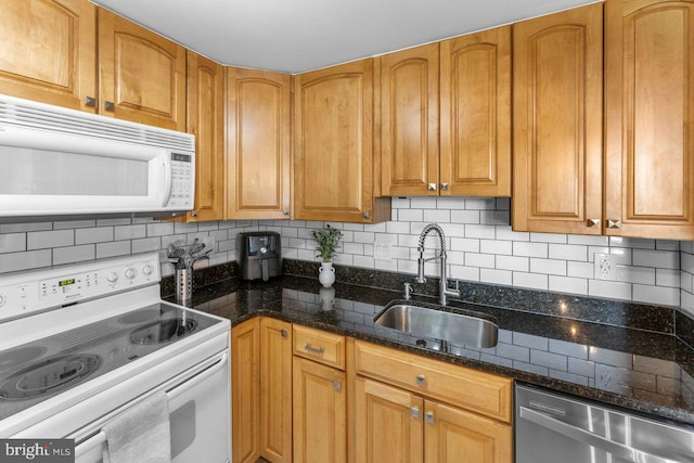 kitchen featuring white appliances, a sink, backsplash, and dark stone countertops