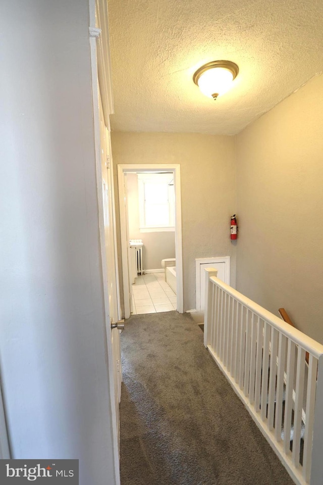 1235 Owen Pl NE, Washington, DC 20002 - hallway featuring an upstairs landing, a textured ceiling, carpet, radiator heating unit, and tile patterned flooring