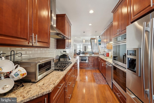 14 E Preston St, Baltimore, MD 21202 - kitchen featuring appliances with stainless steel finishes, wall chimney exhaust hood, light wood-style floors, backsplash, and light stone counters