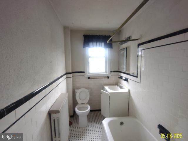 608 Chestnut Hill Ave, Baltimore, MD 21218 - bathroom featuring radiator heating unit, a bath, vanity, toilet, and tile walls