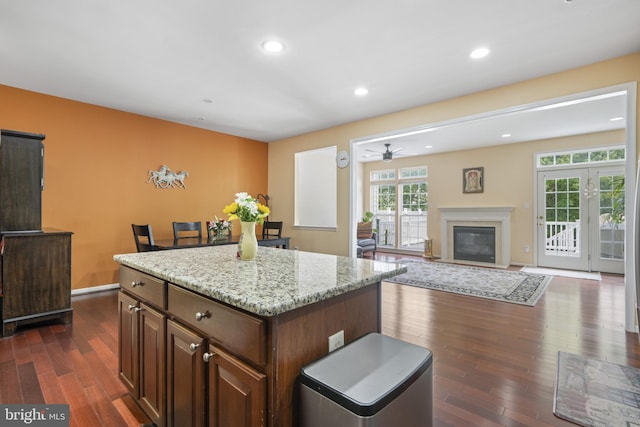 10745 Hillingdon Rd, Woodstock, MD 21163 - kitchen with dark wood finished floors, a center island, a ceiling fan, a fireplace with flush hearth, and light stone countertops
