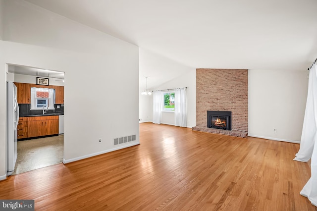 8320 Overmont, Parkville, MD 21234 - unfurnished living room with lofted ceiling, a sink, light wood-style flooring, a brick fireplace, and baseboards
