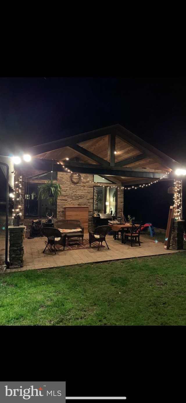 4306 National Pike, Markleysburg, PA 15459 - back of house at night featuring a patio area, a lawn, and stone siding