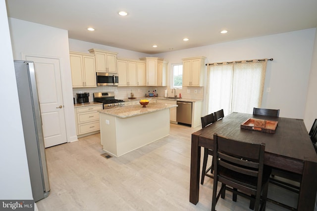 36063 Auburn Way, Millsboro, DE 19966 - kitchen featuring appliances with stainless steel finishes, cream cabinets, a sink, decorative backsplash, and a center island
