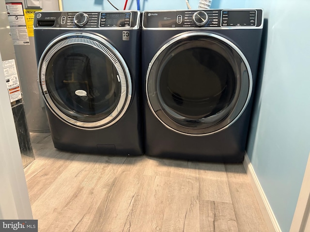 laundry room featuring washing machine and clothes dryer, wood finished floors, water heater, and baseboards