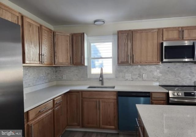 kitchen featuring appliances with stainless steel finishes, a sink, brown cabinets, tasteful backsplash, and dark wood-type flooring