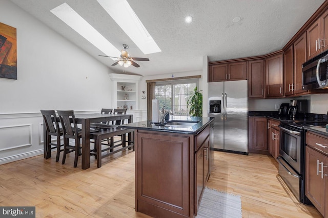 6402 Devonshire Ln, Frederick, MD 21703 - kitchen featuring appliances with stainless steel finishes, a skylight, a sink, light wood finished floors, and a center island with sink