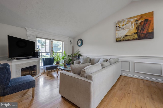 6402 Devonshire Ln, Frederick, MD 21703 - living area featuring lofted ceiling, light wood-style flooring, a glass covered fireplace, wainscoting, and a textured ceiling