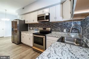 1743 E Oliver St, Baltimore, MD 21213 - kitchen with stainless steel appliances, white cabinets, tasteful backsplash, light wood-type flooring, and hanging light fixtures