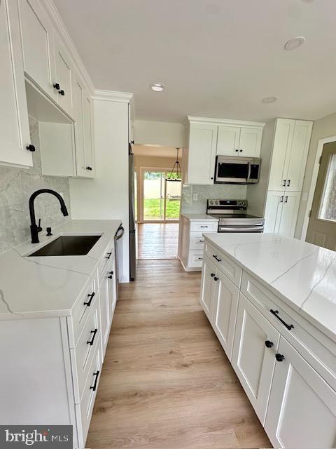 525 E Indian Spring Dr, Silver Spring, MD 20901 - kitchen featuring stainless steel appliances, a sink, white cabinetry, backsplash, and light wood-type flooring