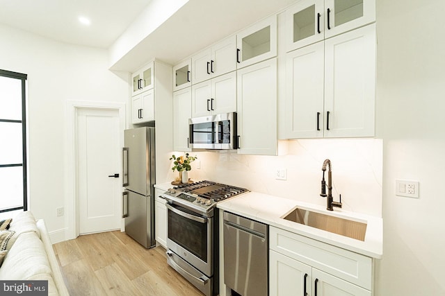 2517 Ontario Rd NW Unit 5, Washington, DC 20009 - kitchen featuring appliances with stainless steel finishes, a sink, light wood-style floors, white cabinetry, and decorative backsplash