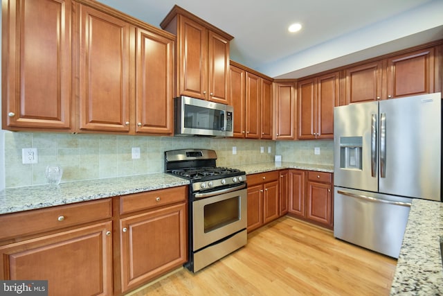 21623 Romans Dr, Ashburn, VA 20147 - kitchen featuring appliances with stainless steel finishes, brown cabinetry, light wood-style floors, light stone counters, and recessed lighting