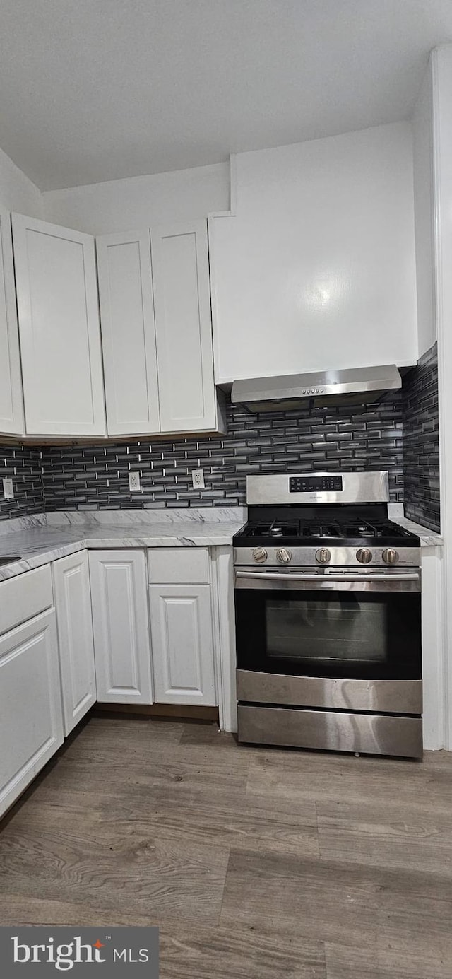 2540 W Silver St, Philadelphia, PA 19132 - kitchen with stainless steel gas stove, wall chimney exhaust hood, white cabinetry, dark wood finished floors, and decorative backsplash