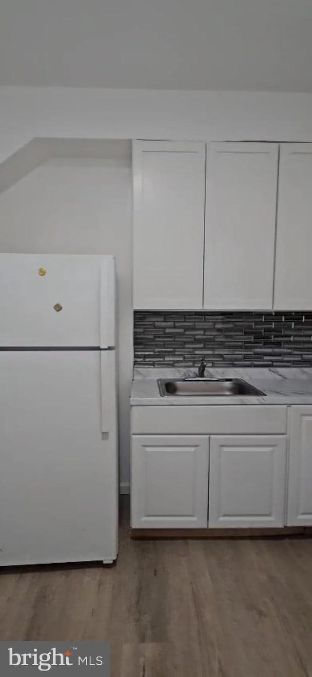 2540 W Silver St, Philadelphia, PA 19132 - kitchen with freestanding refrigerator, a sink, white cabinetry, light wood-style floors, and tasteful backsplash