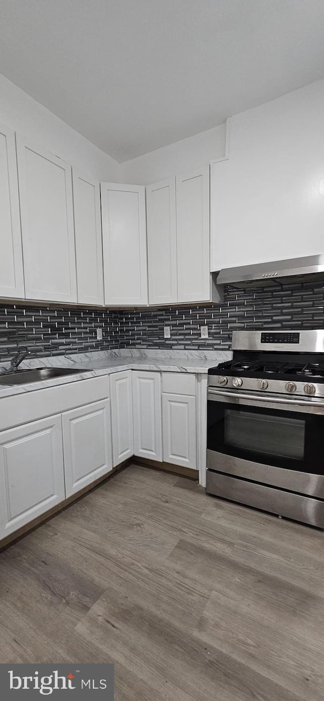 2540 W Silver St, Philadelphia, PA 19132 - kitchen featuring stainless steel range with gas cooktop, white cabinets, wall chimney exhaust hood, light countertops, and backsplash