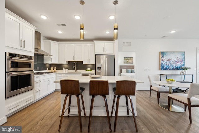 210 Decoverly Dr Unit 407, Gaithersburg, MD 20878 - kitchen featuring appliances with stainless steel finishes, wall chimney exhaust hood, light countertops, white cabinetry, and a kitchen breakfast bar