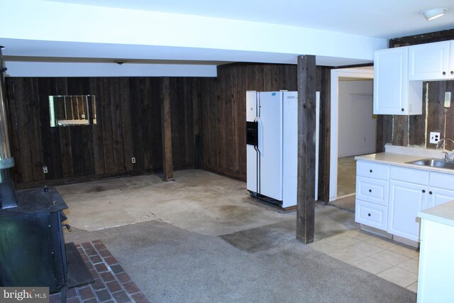 8406 Rainbow Bridge Ln, Springfield, VA 22153 - kitchen featuring white refrigerator with ice dispenser, a wood stove, white cabinets, wooden walls, and light countertops