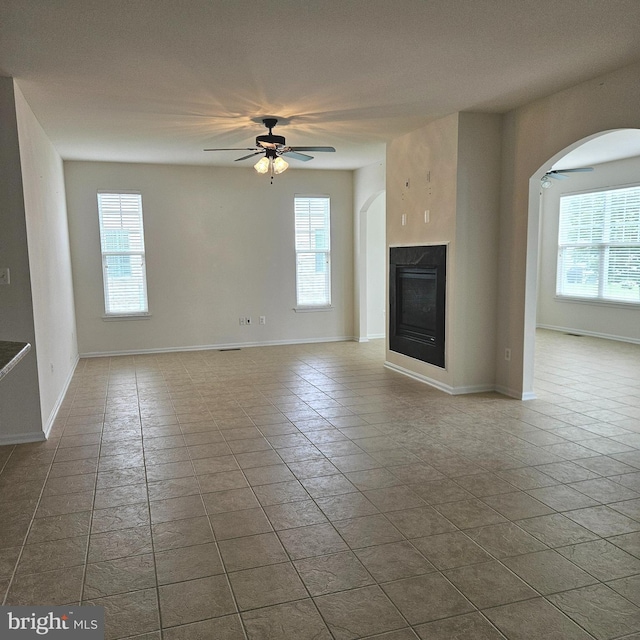 16288 Corkscrew Ct Unit 203, Lewes, DE 19958 - unfurnished living room with ceiling fan, arched walkways, a glass covered fireplace, baseboards, and tile patterned flooring