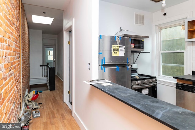 2308 N Park Ave, Philadelphia, PA 19132 - kitchen with stainless steel appliances, wood finished floors, a skylight, healthy amount of natural light, and brick wall