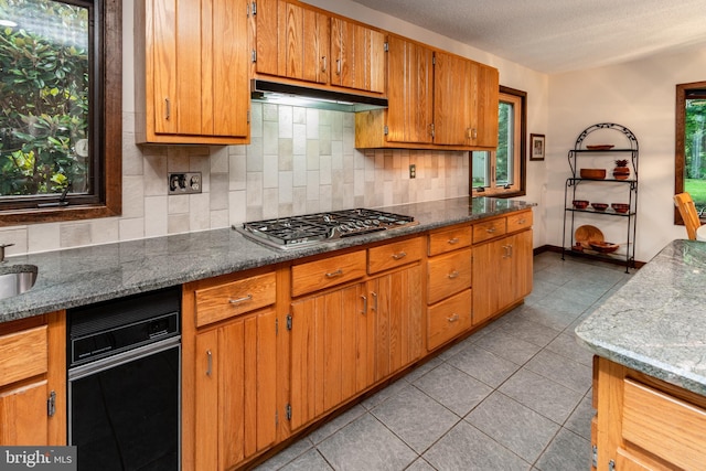 27 Arnold Dr, Princeton Junction, NJ 08550 - kitchen featuring stainless steel gas cooktop, under cabinet range hood, backsplash, light tile patterned flooring, and brown cabinetry