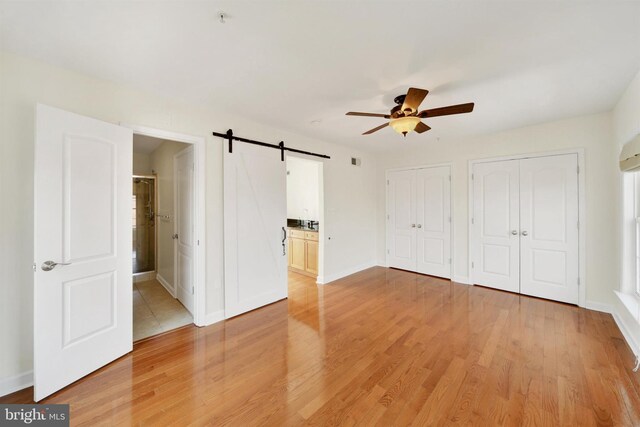1501 Stack St, Baltimore, MD 21230 - unfurnished bedroom featuring a barn door, two closets, light wood-style floors, connected bathroom, and a ceiling fan