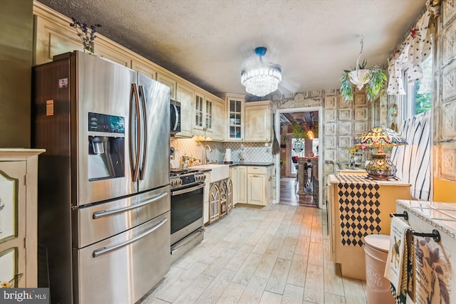 947 Martin Rd, Baltimore, MD 21221 - kitchen with appliances with stainless steel finishes, light wood finished floors, cream cabinets, glass insert cabinets, and a textured ceiling