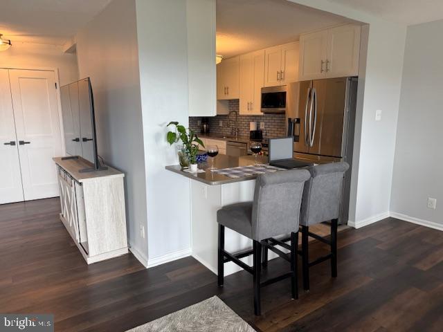 309 Yoakum Pkwy Unit 1809, Alexandria, VA 22304 - kitchen with appliances with stainless steel finishes, tasteful backsplash, dark wood-style flooring, a peninsula, and white cabinets