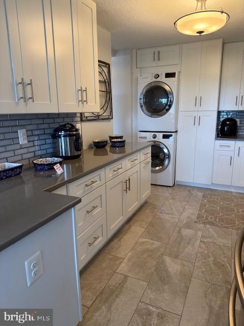 309 Yoakum Pkwy Unit 1809, Alexandria, VA 22304 - kitchen with stacked washer / dryer, white cabinets, backsplash, dark countertops, and a textured ceiling