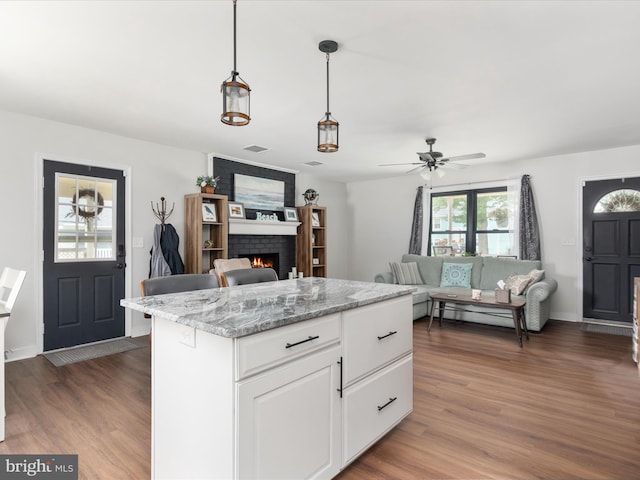 29 8th St, Colonial Beach, VA 22443 - kitchen featuring a brick fireplace, wood finished floors, open floor plan, white cabinets, and decorative light fixtures