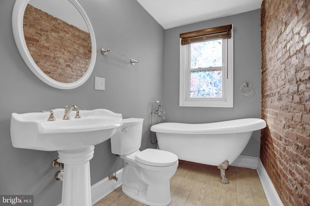 503 W 27th St, Baltimore, MD 21211 - bathroom with a freestanding bath, wood finished floors, baseboards, brick wall, and toilet