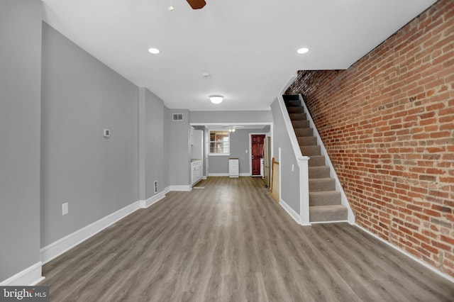 503 W 27th St, Baltimore, MD 21211 - unfurnished living room with brick wall, a ceiling fan, wood finished floors, stairway, and baseboards