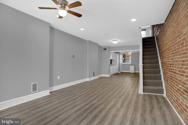 503 W 27th St, Baltimore, MD 21211 - unfurnished living room featuring brick wall, wood finished floors, stairway, ceiling fan, and baseboards