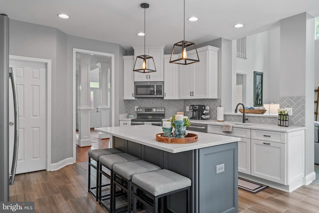 6000 Clairemont Dr, Owings, MD 20736 - kitchen featuring stainless steel appliances, a sink, white cabinets, a breakfast bar, and wood finished floors
