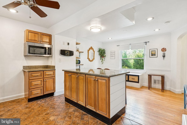 5721 Greenspring Ave, Baltimore, MD 21209 - kitchen with stainless steel microwave, brown cabinets, arched walkways, ceiling fan, and baseboards