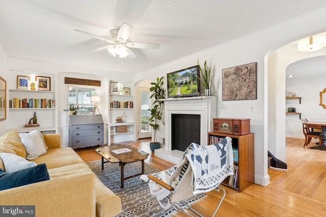 5721 Greenspring Ave, Baltimore, MD 21209 - living area with arched walkways, wood finished floors, a ceiling fan, and a fireplace with raised hearth